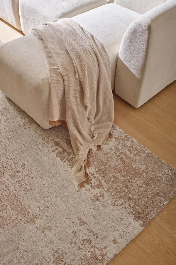 Modułowa jasna sofa z narzutą, ustawiona na beżowym dywanie